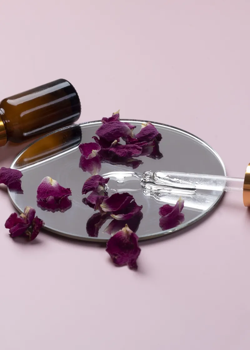 Buteleczka serum z pipetą i płatkami róż na lustrze